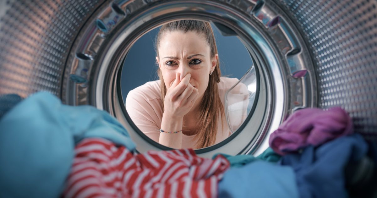 Woman staring at the laundry in the washing machine and holding her nose