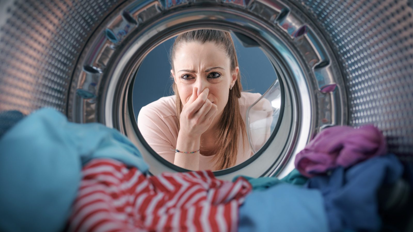Woman staring at the laundry in the washing machine and holding her nose